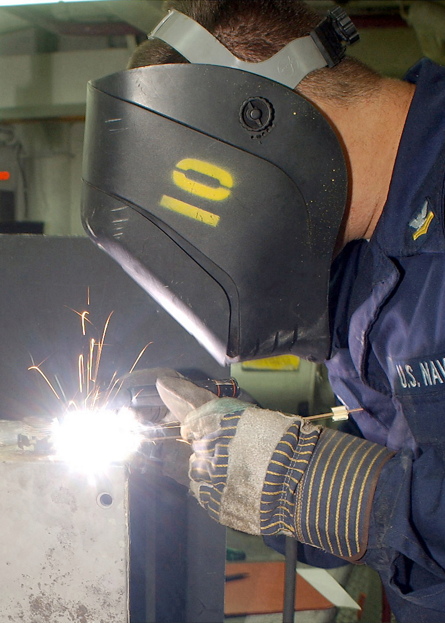 A welder in protective gear works inside a cramped, enclosed steel compartment