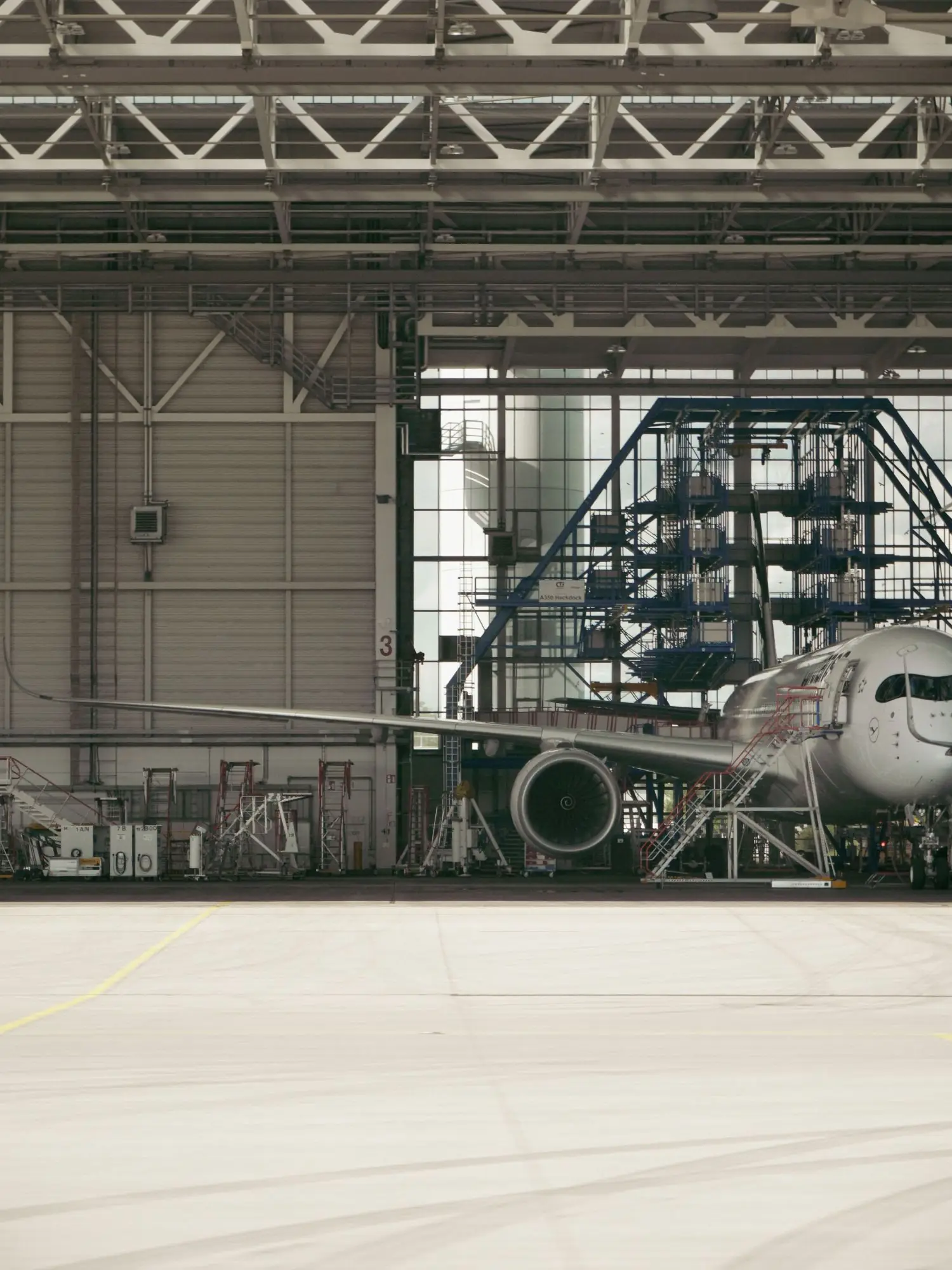 A wide-body airliner with maintenance stairs and work platforms inside a hangar