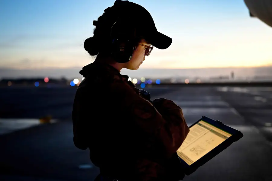 An aircraft maintainer reviewing a technical order on a tablet at dusk