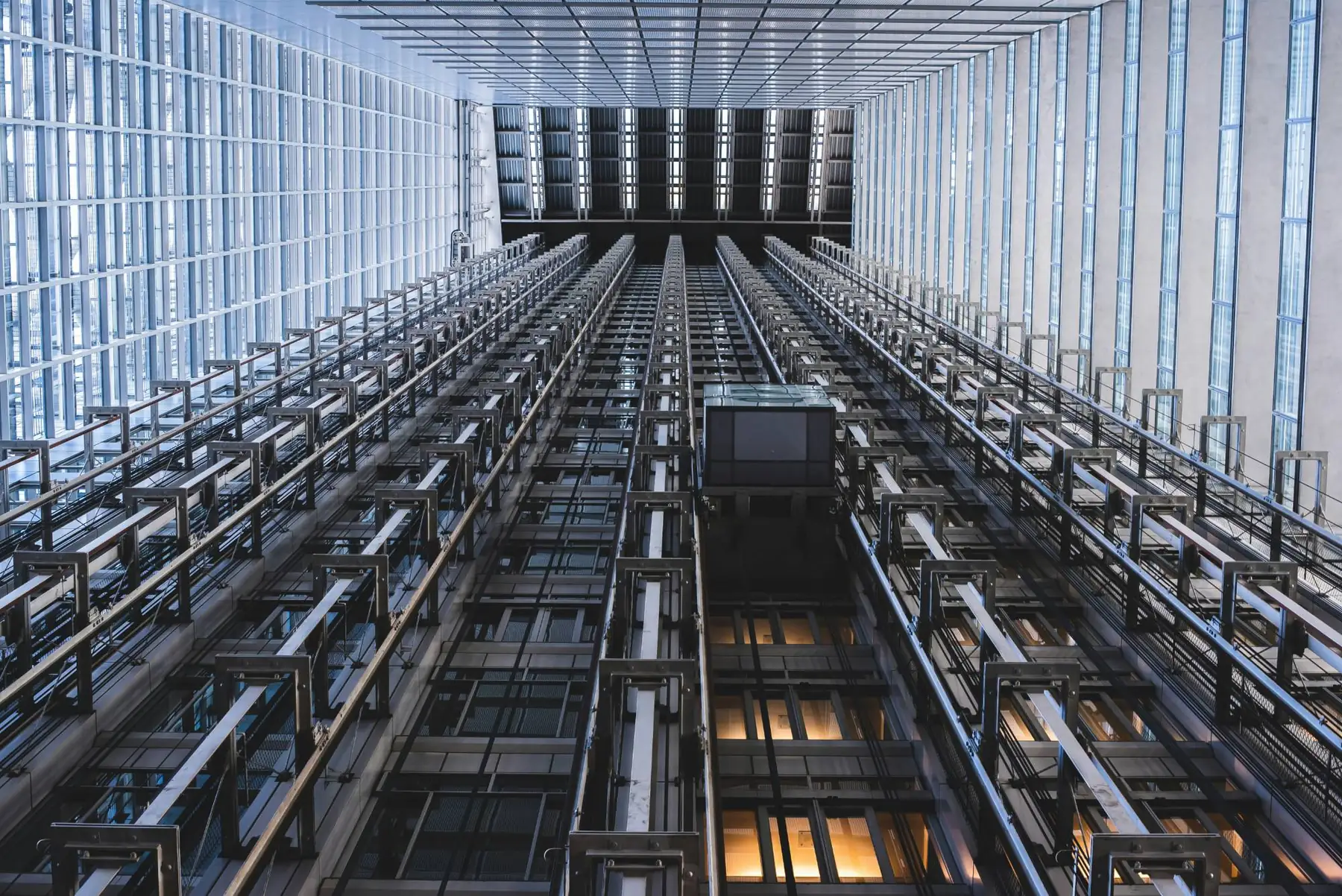 Looking up an atrium of elevator shafts, guide rails and a glass elevator car