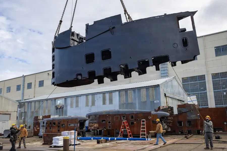 A crane lifting a large steel structure at a shipyard while workers keep their distance