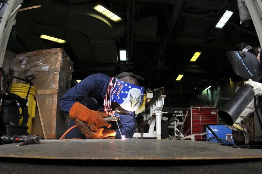 A welder at work with a fire watch standing by