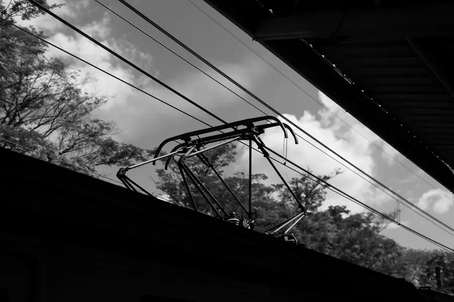A pantograph on a train roof against the sky, in black and white
